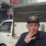 Šis vīrs izlēma, ka ar to vien, ka ir albīns nebūs gana. Labi, varbūt viņš nav albīns, varbūt tā ir kāda ādas saslimšana, nezinu. Labāk pilnam komplektam piemetīšu klāt spilgti oranži nokrāsotus matus, bārdu un pat uzacis. Nice. Atvainojos, ka fokuss uz fonā esošo auto, bildēju ar automātu, un divas reizes bildēt šo kungu nokautrējos/nobaidījos - re, kas viņam uz cepures rakstīts! Tas nozīmē, ka rokā ierocis.