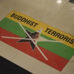 Dodamies tālāk, un terorisms seko mums pa pēdām. Šoreiz grīdas uzlīmes veidā kādā no elektronikas veikaliem (tā kā esam skopi, regulāri pērkam lētās austiņas, jo iepriekšējās lētās austiņas kārtējo reizi ir saplīsušas. Uz šo brīdi mēs noteikti būtu jau ietaupījuši, vienreiz nopērkot dārgākas, bet kvalitatīvākas austiņas). Reku divi vārdi, kas līdz šim man kaut kā galīgi neasociējās viens ar otru - budisms un terorisms. Fonā redzams Mjanmas karogs. Pēc tam papētīju vairāk, jā, izrādās patiešām Mjanmā notiek vardarbīga musulmaņu kopienas diskriminācija, bet ko nu runāt par to tagad. Visam savs laiks.