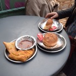 Turpat ielas malā arī ieturam pusdienas. Jau ierastais veģetārais, ar kartupeļu kotleti pildītais burgeris un katram pa samosai - tas ir tāds ar visādiem dārzeņiem pildīts mīklas trijstūrītis, kurš tiek izvārīts eļļā. Šī bija pirmā reize, kad baudīju samosu, tāpēc man uzreiz radās iespaids, ka tas ir kaut kas, kas man negaršo. Pēc vairākām nedēļām, kad pamēģināju samosu vēlreiz, izrādījās, ka pie vainas nevis pati samosa, bet gan ēstuve, kurā to pasūtījām, un patiesībā samosas ir ļoti, ļoti garšīgas!!! Tas ir, ja to labi (un galvenais ar mīlestību) pagatavo.