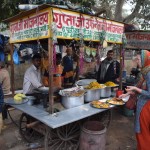 Autobuss mūs nogādā līdz tai pašai New Delhi stacijai, bet no otras puses, tāpēc neko te nesaprotam, kur jādara kas, kur jāēd, kur tualete, neko!!! No rīta, protams, brokastis nepaēduši (labāk līdz pēdējam brīdim gulēt, un tad mudīgi skriet, lai pēdējā brīdī paspētu nokārtot vīzas), esam velnišķīgi izsalkuši, tāpēc apstājamies pie pirmā, lai arī aizdomīgā, stendiņa un pasūtām ēdienu. Jā, no šādiem stendiņiem bieži vien jāpasūta tikai skaits: Man, lūdzu, divus ēdienus. Ēdienkartē ir tikai viens objekts un neko citu jau arī nepasniedz.