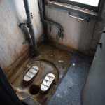 Šī ir tualete, šeit viss ir slapjš ar nezkādiem šķidrumiem (šķidrumu izcelsme nav pat nojaušama, haha), drausmīgi smirdīgs un visādi citādi patīkams. Starp citu, naktīs, kad jādodas uz sapņu pasauli, ne visiem pietiek vietas vagonos uz grīdām, un tiešām šad tad esmu novērojis vienu otru guļam šeit. Ne jau gluži virs tā cauruma, bet turpat blakus, kas vienalga ir drausmīgi pretīgi. Un vēl pretīgāk ir tad, kad tādam lepnam gultasvietas biļetes turētājam kā man nav, kur naktī pačurāt, hehe.