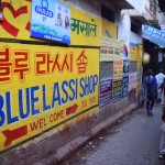 Jau pirms ierašanās pilsētā biju salasījies Lonely Planet grāmatā, ka "Best Lassi in Varanasi" esot bodītē, kas saucas Blue Lassi Shop. Tā kā Varanasi vecpilsēta ir visai grūti navigējama - mazas, līkumotas, krustām-šķērsām ieliņas - biju izdomājis, ka gan jau vēl atradīsim laiku tajā bardakā atrast arī Blue Lassi, un tas nepavisam nav obligāti jāizdara šodien. Bet izrādās, ka Lonely Planet grāmatas lasītāju nestie ienākumi ir atļāvuši Blue Lassi saimniekiem izvērst pamatīgu mārketingu - šādas te lielākas un mazākas zīmes ar norādēm, kurā virzienā jāiet, izvietotas teju pa visu vecpilsētu. Tiešām pat 500 un vairāk metru attālumā no pašas bodītes! Nu, ja jau zīmes ir, tad iesim un skatīsimies uzreiz.