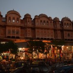 Tā, no vecpilsētas esam ārā, bez kazām tur nebija nekā daudz cita, ko redzēt. Tagad ir jau tumšs, bet domāju, ka vēl var saskatīt ēku dīvaino rozā krāsu. Džaipūras iesauka/sauklis ir Pink city (rozā pilsēta), pastāstīšu, kāpēc. Kad deviņpadsmitā gadsimta nogalē Indijas tūrē devās Karaliene Viktorijas un Velsas princis, viņi apmeklēja arī Džaipūru, un centīgais vietvaldis Maharadža Rams Singhs izlēma, ka visprātīgāk būtu nokrāsot visas oficiālās ēkas viesmīlības krāsā. Es nezinu, kāpēc, bet rozā laikam ir viesmīlības krāsa. Nu, lūk, būdami paklausīgi un lojāli pilsoņi, Maharadžas piemēram sekoja arī parastie pilsētnieki, līdz drīz viss pilsētas centrs nokrāsojies rozā. Pēc karalienes vizītes, protams, neviens vairs nepārkrāsoja ēkas atpakaļ iepriekšējā krāsā, nav ko lieki tērēties. Tā arī iegājās tradīcija un nosaukums. Mūsdienās jau tradīcijas nevienam vairs īpaši nav prātā (īpaši Indijā, kur vienīgā parasto ļaužu tradīcija ir nauda), tāpēc noteiktām ēku grupām ar likumu ir noliegts krāsoties citā krāsā, izņemot rozā.